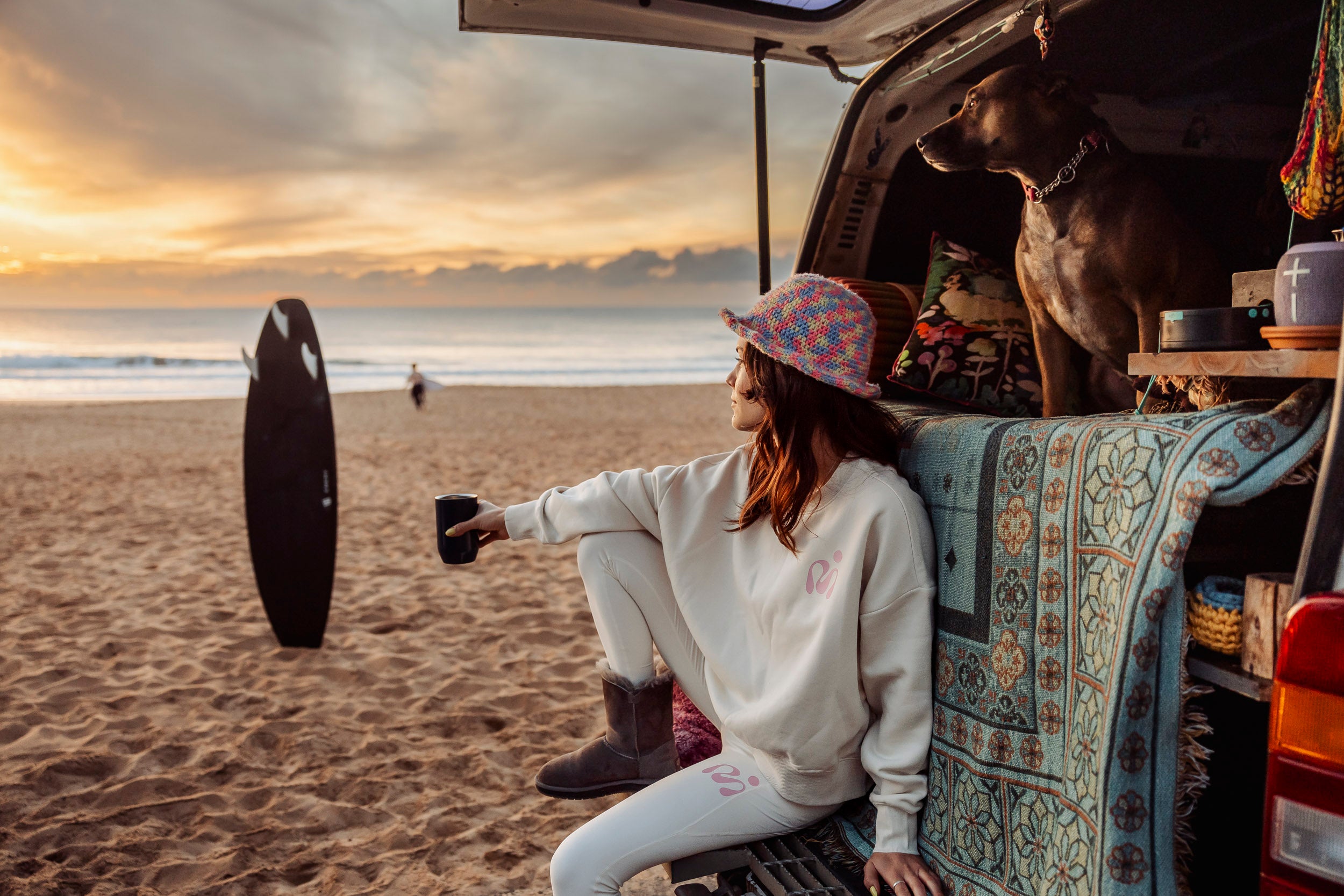 vanlife cool girl with dog looking at sunrise on the beach